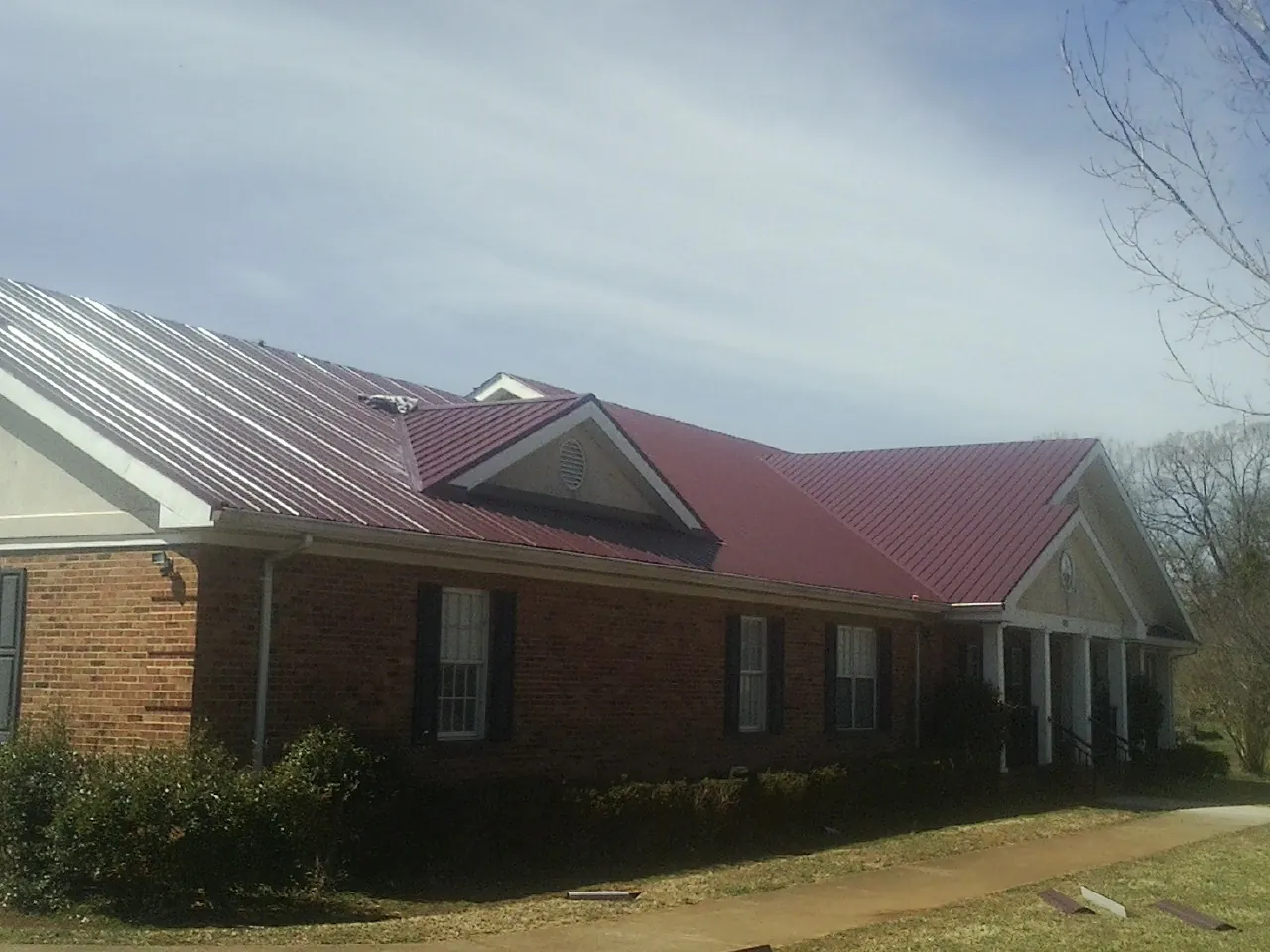 Red metal roof with gabled entries on a long brick building, from a Hail Damage Roof Repair job in Pearl City