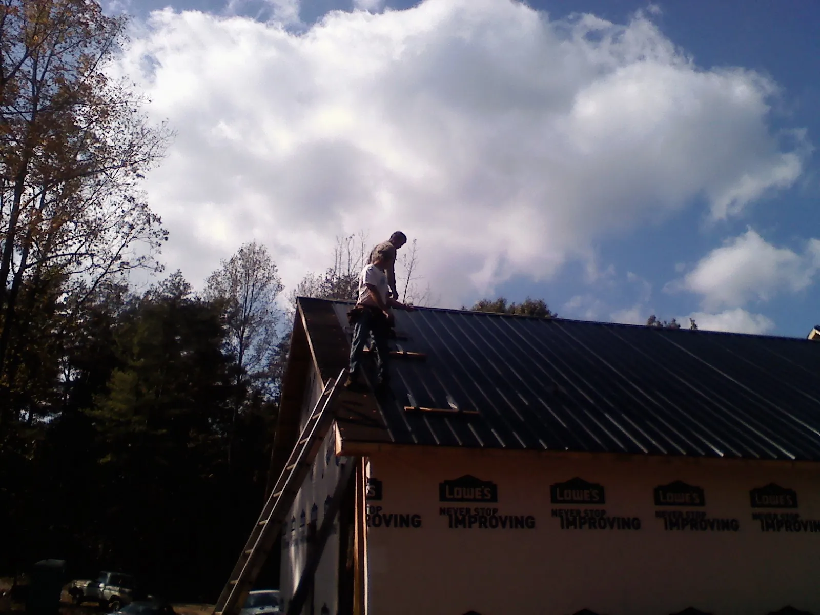 Roofer fastening dark metal panels high against a cloudy sky, from a Roof Inspection job in Pearl City