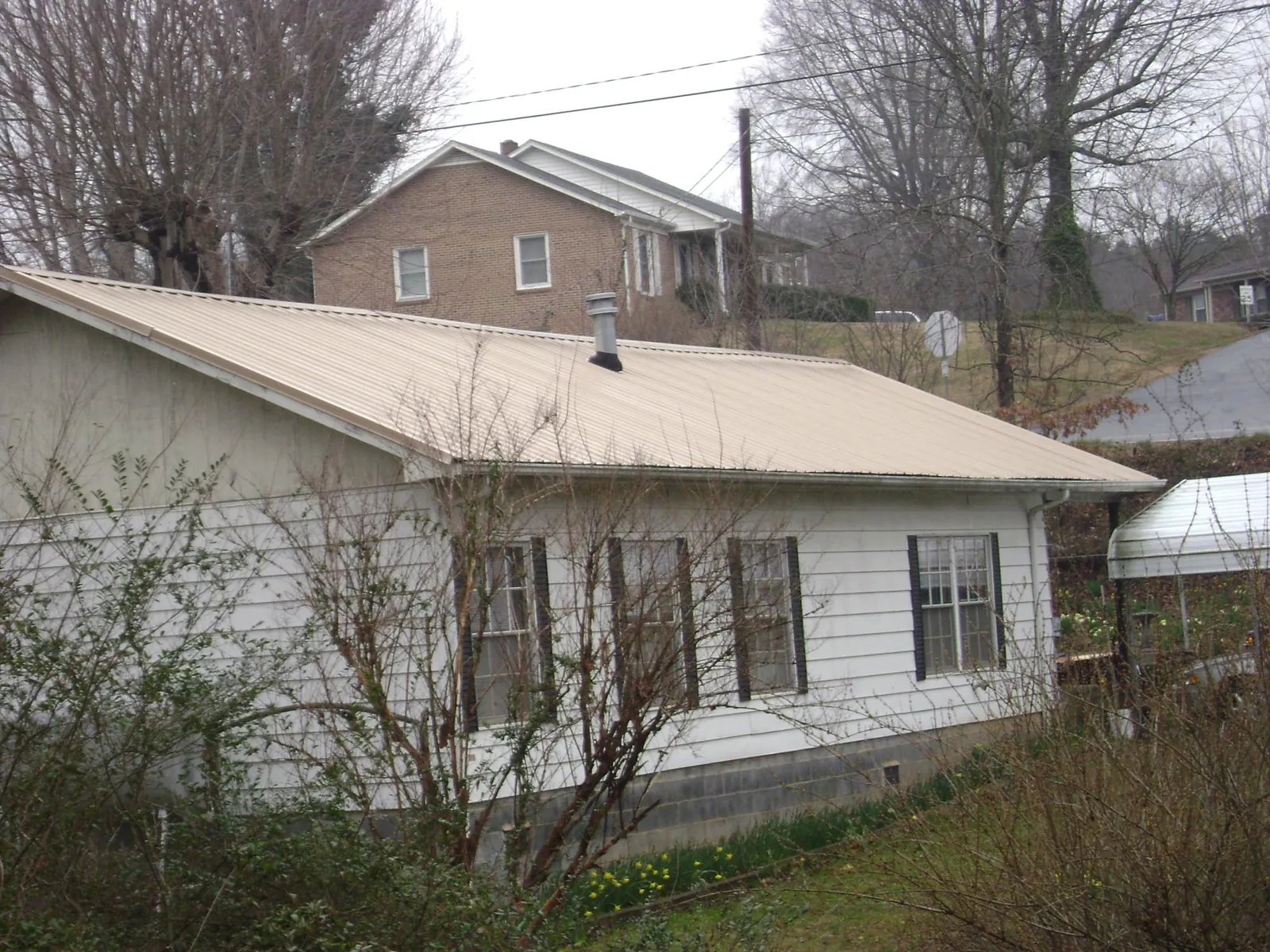 Tan metal roof on a white sided house set into a hillside — Commercial Roofing by Roofing Brothers in Pearl City