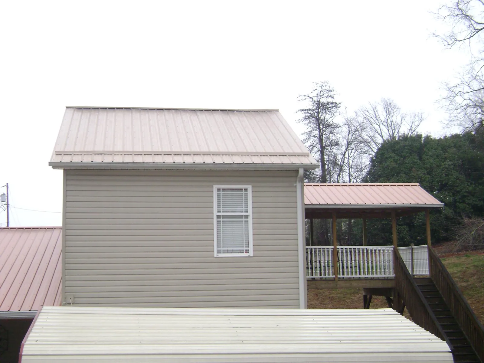 Tan metal roofs on a two story addition and attached porch, from a Roof Replacement job in Pearl City